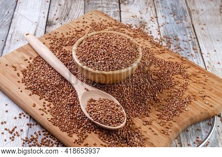 Scattered Buckwheat. Buckwheat In A Wooden Bowl And Spoon Lies On A Wooden Table. Scattered Buckwhea