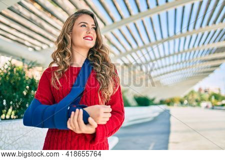 Young blonde girl smiling happy injuried with arm sling standing at the park.