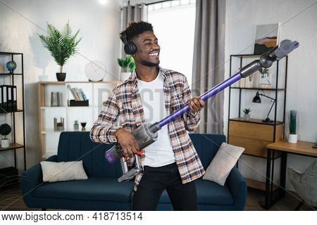 Cheerful Afro American Man Imitating Play On Guitar Using Handheld Vacuum Cleaner. Happy Young Man L