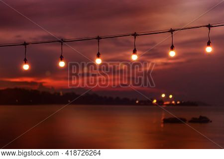Blurred Bokeh Light On Sunset With Yellow String Lights Decor In Beach Restaurant, Tranquility Of Se