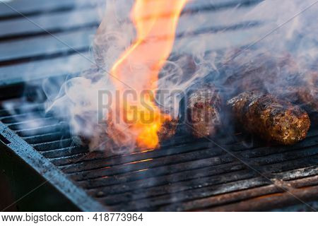 Preparing Meat Rolls Called Mici Or Mititei On Barbecue. Close Up Of Grill With Burning Fire With Fl
