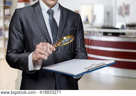 Criminal Investigation Study Concept. Lawyer Examining A Document With A Magnifier On A Blurred Back