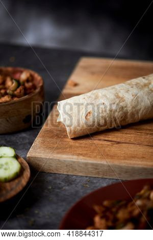 a durum or a burrito, filled with chicken meat cooked with different vegetables such as onion or red and green pepper, and fresh lettuce and cucumber, on a table