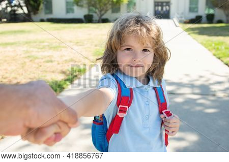 Little Boy With Backpack Holding Parent Fathers Hand On Blurred School Building Background. Child Wi