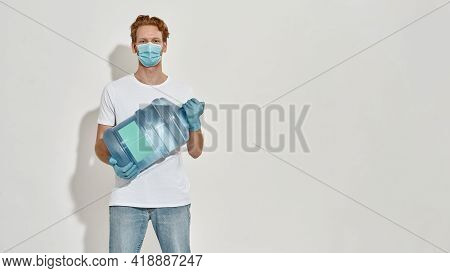 Horizontal Picture Of A Young Deliveryman Holding Big Bottle Of Water, He Is Standing Over The White