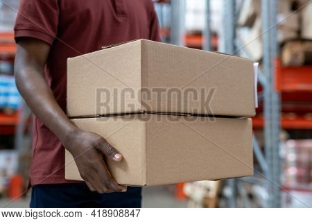 Close-up of unrecognizable Black mover carrying two cardboard boxes along stockroom