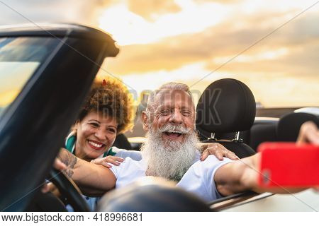 Happy Senior Couple Having Fun On New Convertible Car Roadtrip Taking Selfie With Mobile Smartphone 