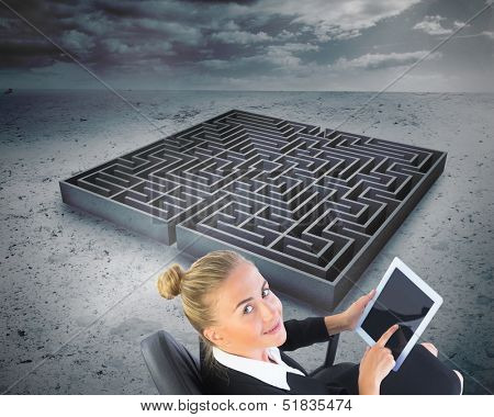 Composite image of blonde businesswoman sitting on swivel chair with tablet with a big maze in the background