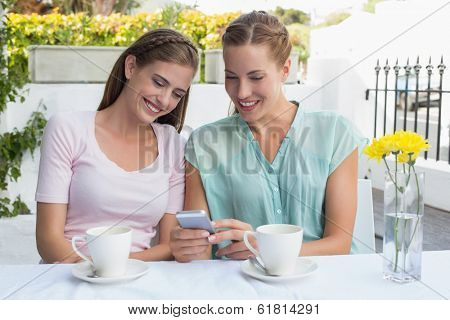 Two happy female friends reading text message at the coffee shop