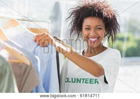 Portrait of a smiling female volunteer by clothes rack