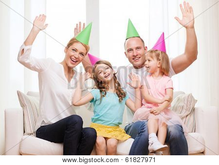 celebration, family, holidays, children and birthday concept - happy family with two chldren in hats waving hands at home