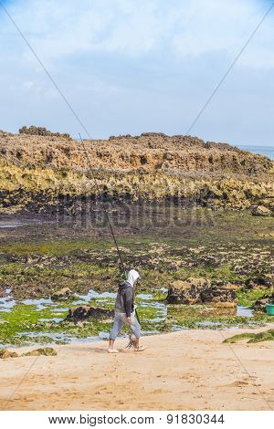OUALIDIA, MOROCCO, APRIL 6, 2015: Fishermen with rod and caught octopus walks along beach