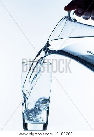 pure water is emptied into a glass of water from a jug. fresh drinking water