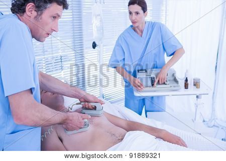 Medical team resuscitating a man with a defibrillator in hospital room