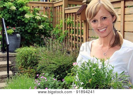 Smiling fifty year old lady gardener outside in the garden holding a pack of lobelia. 