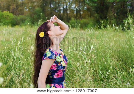 Beautiful young woman standing in a forest clearing among the tall grass and lifting her head looks at the sky