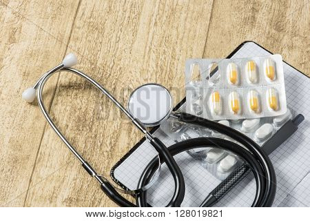 stethoskope on wooden desk with pills pencil and notebook copy space