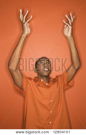 ชายหนุ่ม African-American ทิ้งแขนของเขาขึ้นในอากาศการสวมใส่เสื้อผ้าสีส้มบนสีส้ม backgro