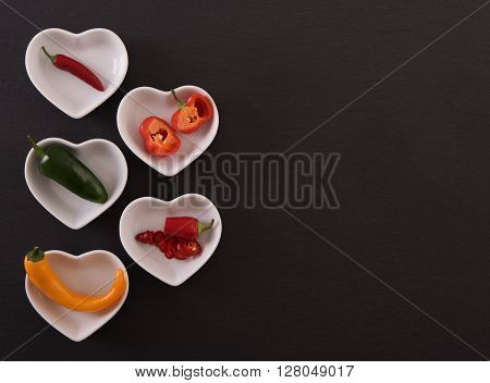 Different chili peppers in white bowls, black stone background