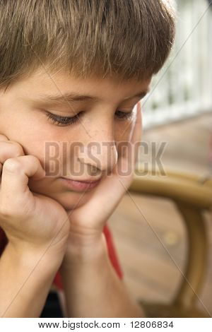 Portrait of Caucasian pre-teen boy with chin in hands looking down.