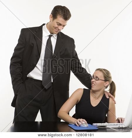 Mid-adult caucásico hombre acosador sexual mujer sentada en la computadora.