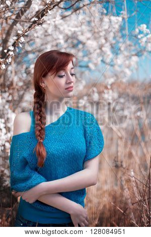 The beautiful red-haired girl stand at the blossoming apple-tree in a grass. The girl has braided a braid. The girl is dressed in an easy jacket.