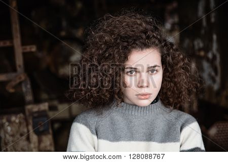 The young woman with the shining eyes looks in a camera. The girl is dressed in a sweater. Girl has magnificent curly hair