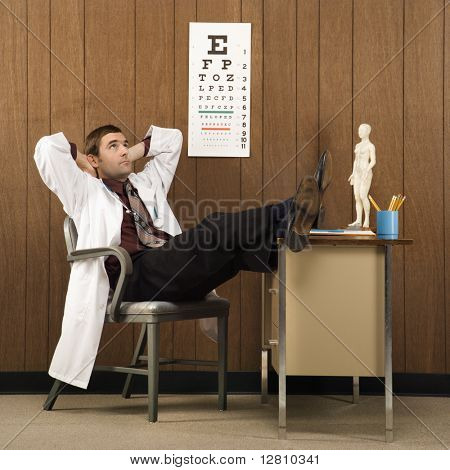 Mid-Adult kaukázusi Férfi orvos az asztalon fekvő kézzel a fej és a lábak, a pult mögött.