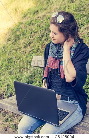 Young woman rubbing her neck while working on a laptop. Millenial working in a park.