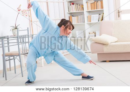 Beautiful woman doing qi gong tai chi exercise or reiki wearing professional, original Chinese clothes at home