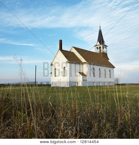 Small rural church in field with chipped wood siding.
