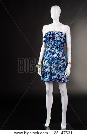 Short blue dress without straps. Strapless floral dress on mannequin. Summer clothing on black background. Woman's vintage style garment.