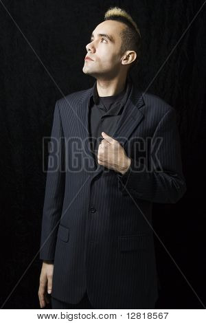 Caucasian man in suit with mohawk  standing posed against black background.