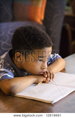 Retrato de menino com a cabeça nos braços com livro na frente.