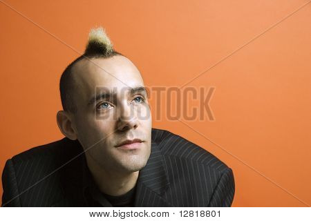 Caucasian man in suit with mohawk against orange background.