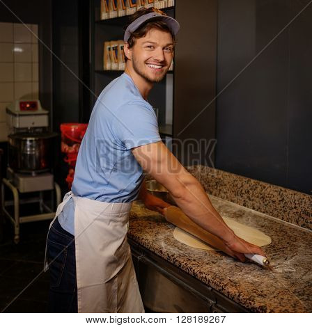 Handsome pizzaiolo rolling dough with rolling-pin.