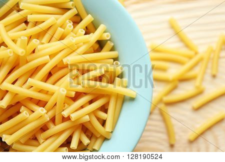 Dry maccheroni pasta in blue plate on wooden table