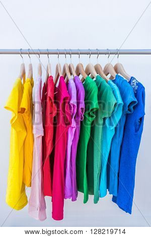 Fashion clothes on clothing rack - bright colorful stand of rainbow selection of t-shirts. Choice of trendy female wear on hangers in store closet or spring cleaning concept. Summer home wardrobe.
