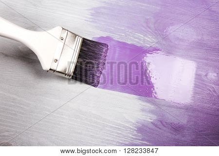 Painting white wooden surface with white paintbrush and violette of lavender color.