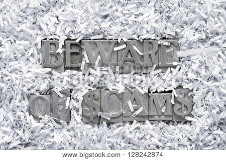 beware of scams phrase made from metallic letterpress type inside of shredded paper heap