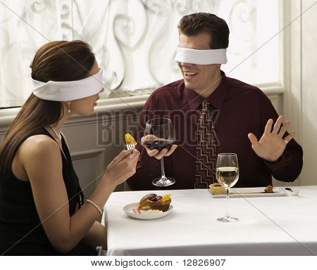 Střední dospělý Kavkazský pár stravování v restauraci s Zavázaný oči nad oči.
