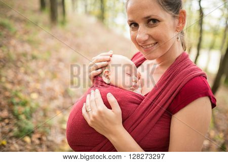 Mother carrying her cute baby daughter in sling, outside in autumn nature
** Note: Shallow depth of field