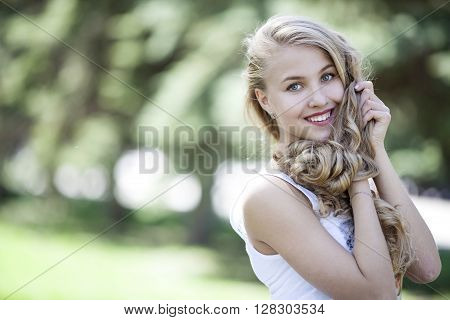 Portrait of beautiful happy girl with long blond hair on the background of green nature summer day