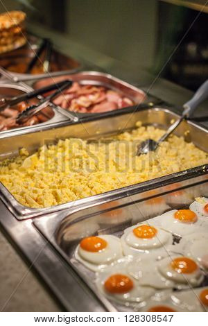 Hot counter containing warm breakfast items such as scrambled or fried eggs, bacon, sausages and others in a self service restaurant in a hotel