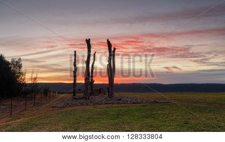 A beautiful winter sunset with rich red hues over rural Penrith with views to Blue Mountains Australia. In the foreground gnarled tree trunks rise from the stony ground