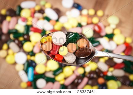 Colorful medical pills on teaspoon and capsules or supplements for therapy in background concept of treatment and health care