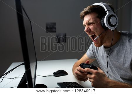 technology, gaming, entertainment, let's play and people concept - screaming young man in headset with controller gamepad playing computer game at home and streaming playthrough or walkthrough video