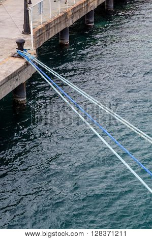 Ships ropes tied to rusty iron bollard on concrete pier