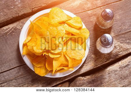 Chips with salt and pepperbox. Pepperbox and chips on table. Simple recipe of potato chips. Popular junk food and spices.