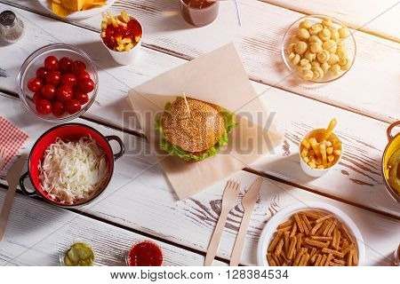 Burger, tomatoes and champignons. Mushroom bowl, burger and pepperbox. Picnic food on white table. Delicious weekend lunch.